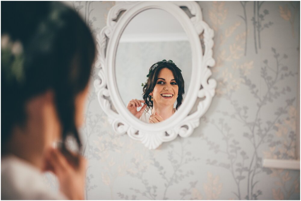 Bride puts her earrings on in the mirror on her wedding morning.