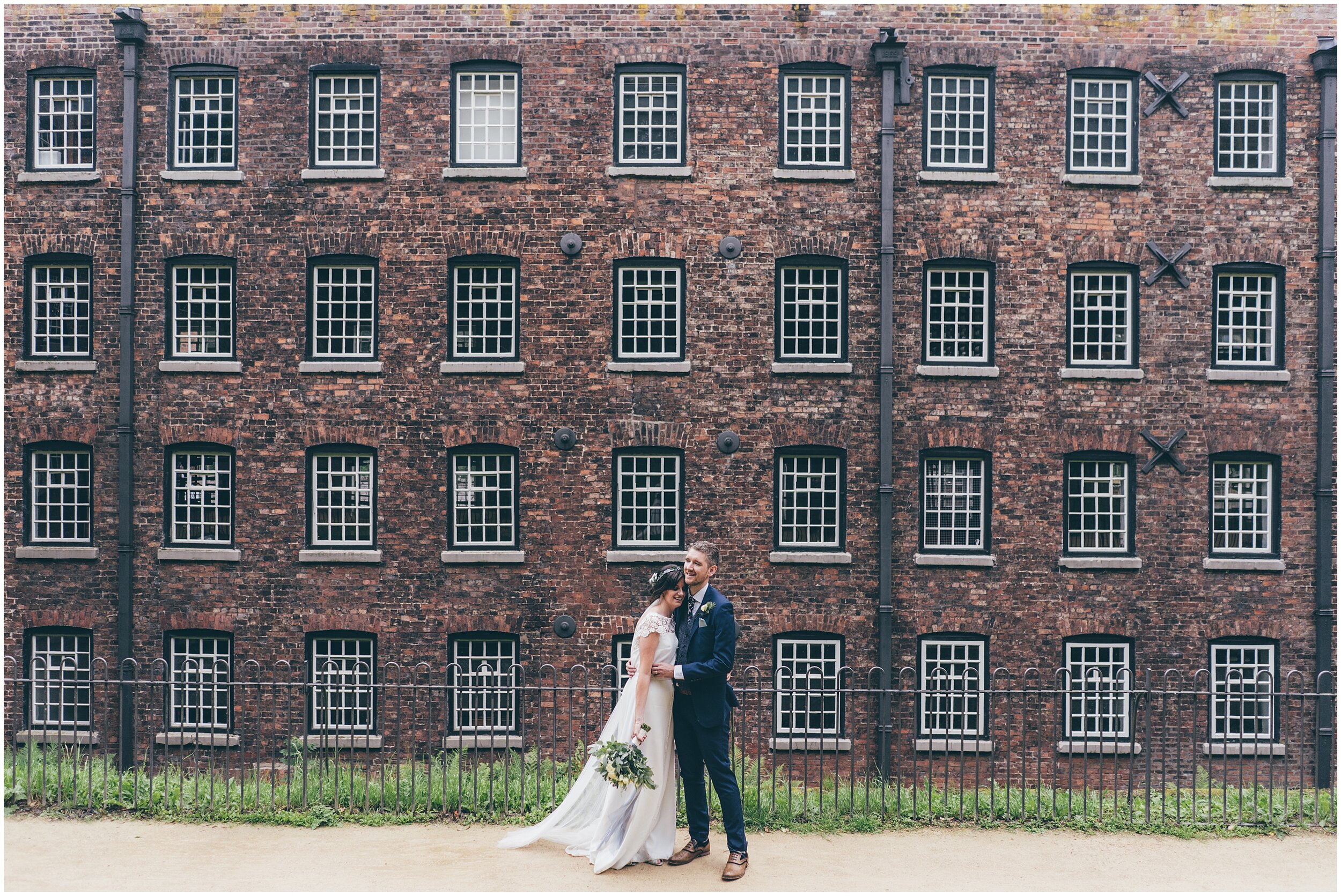 Bride and groom stand at the front of Quarry Bank Mill on their wedding day.