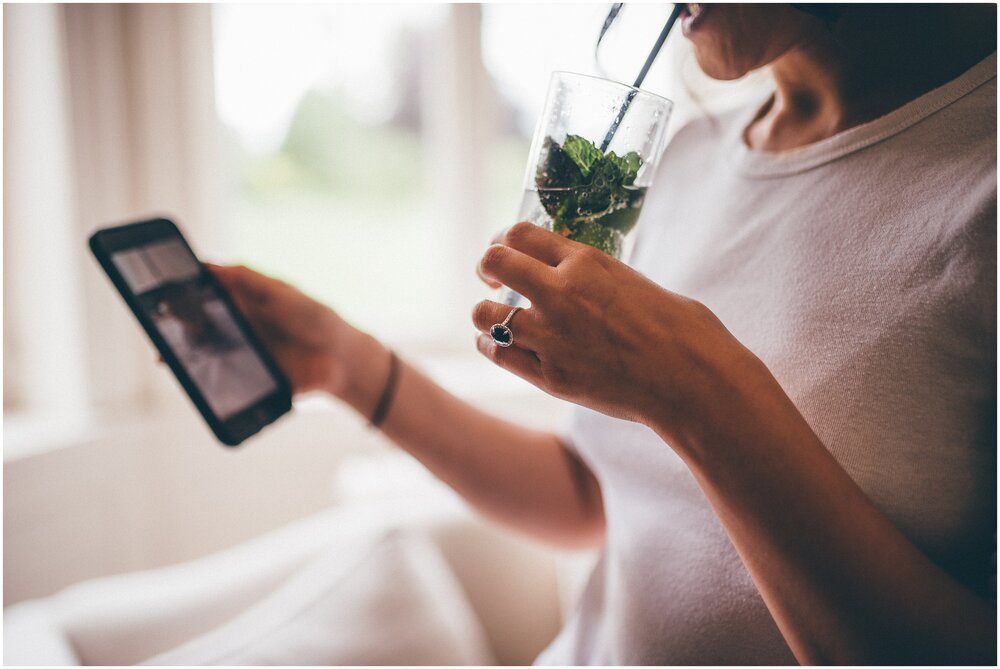 Bride checks her phone whilst drinking a mojito. Her sapphire engagement ring sparkles.