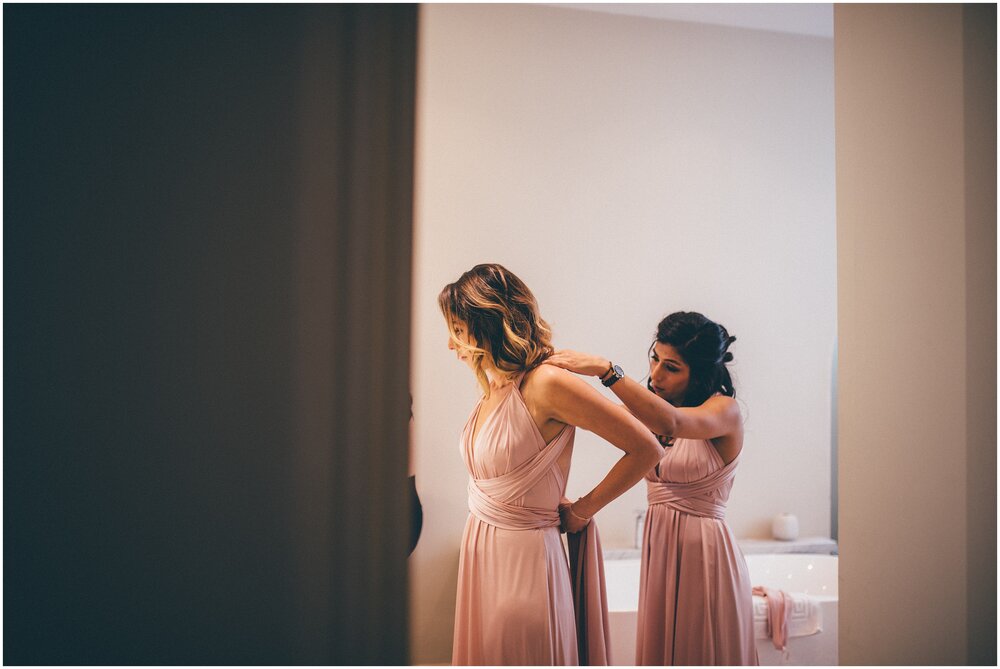 Bridesmaids help each other into their pale pink multiway dresses ahead of the wedding at Chippenham Park Gardens