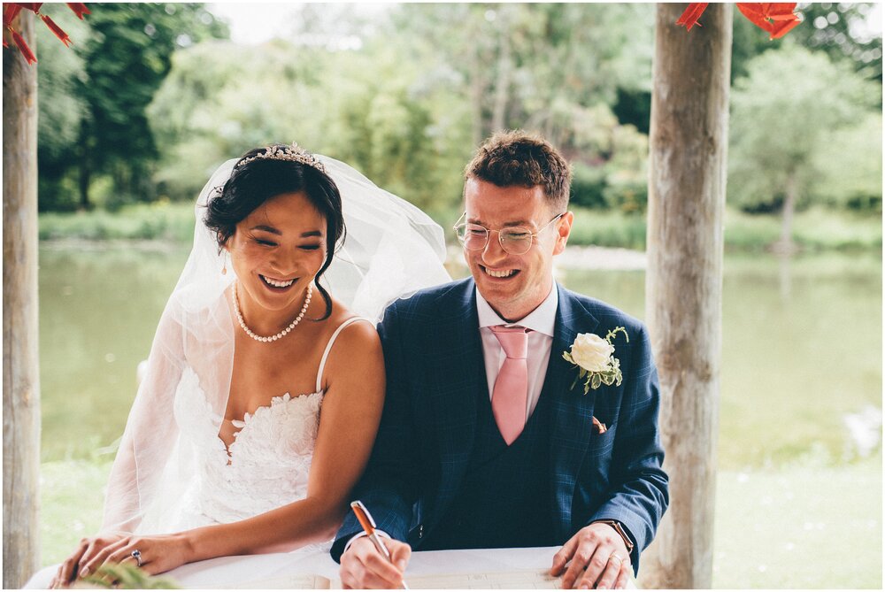Newlyweds laugh as they sign the register at their outdoor wedding ceremony.