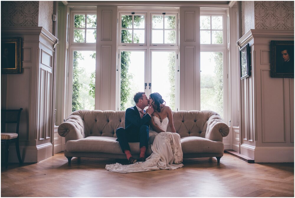 Cute couple on their wedding day share a kiss whilst sat on the sofa at their Cheshire wedding venue.