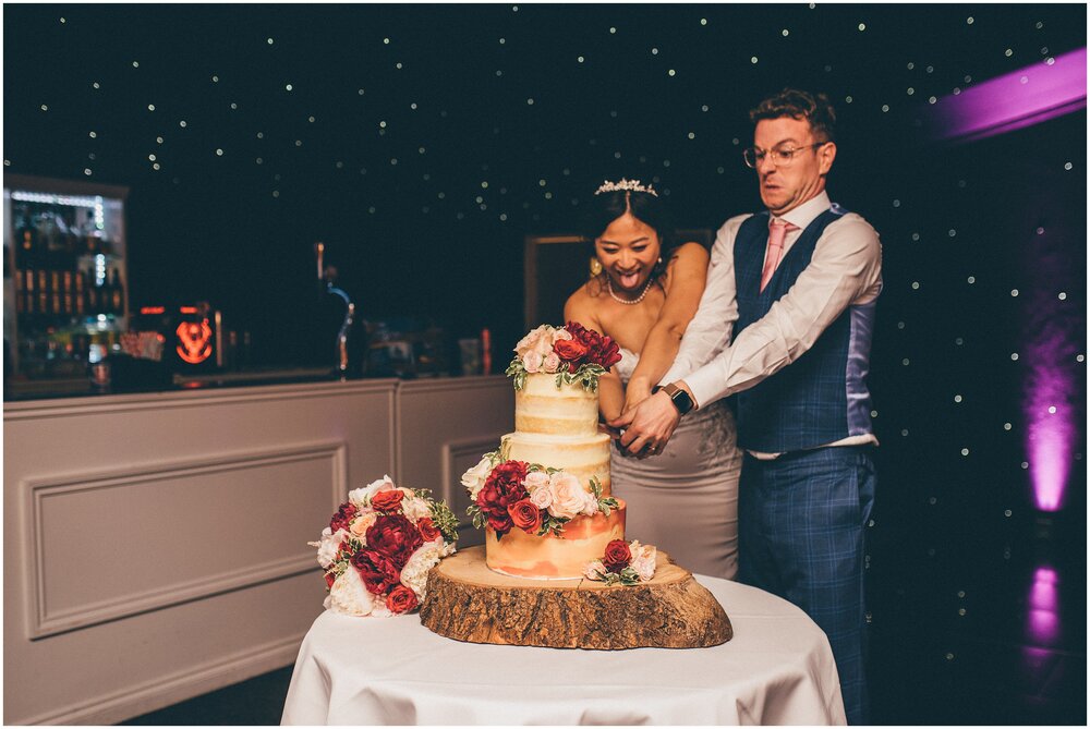 Bride and groom cut their wedding cake, which is a naked iced wedding cake with flowers on at Cheshire wedding venue.