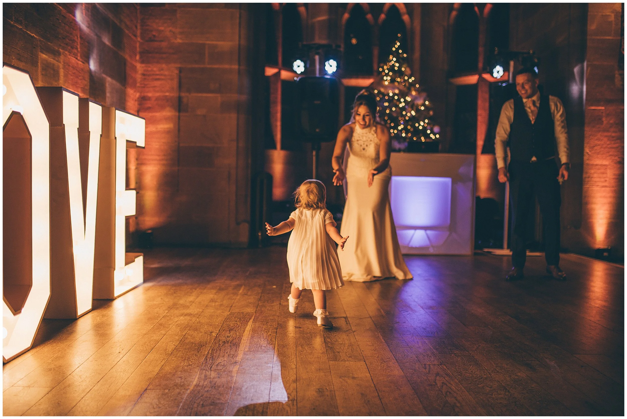 Bride and groom's daughter runs to them at Peckforton Castle in Cheshire