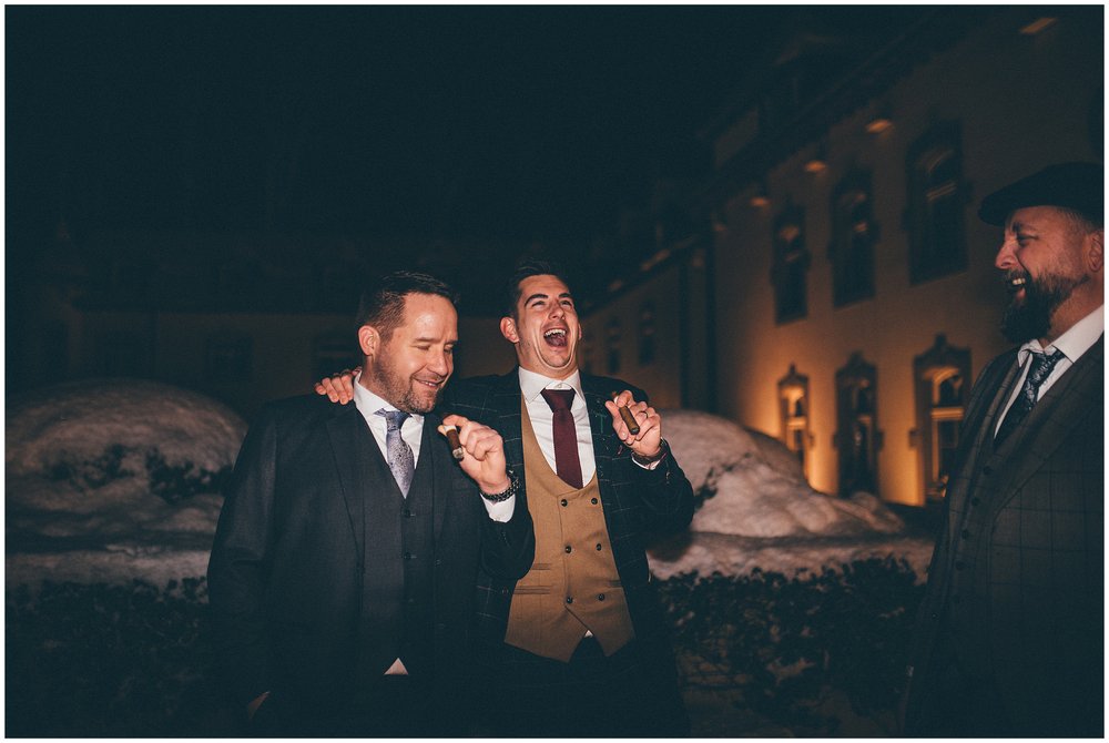 Groom and his friends smoke cigars outside in the snow at Luxembourg wedding