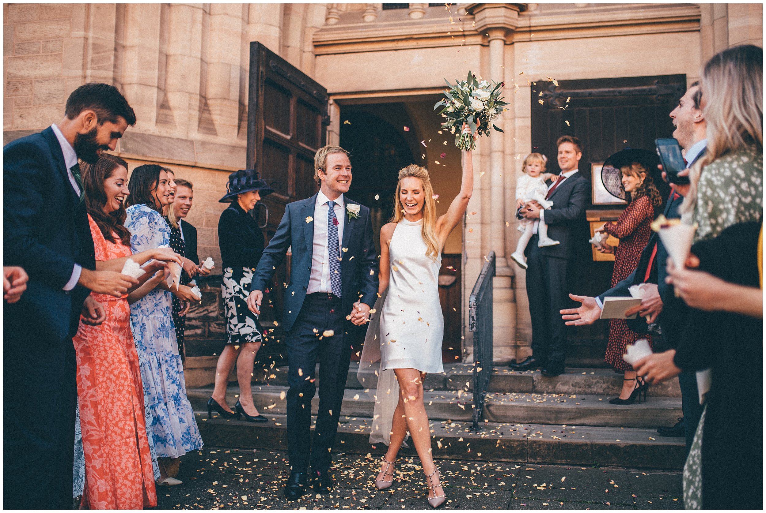 Bride waves her bouquet in the air as guests throw confetti at the newlyweds in Chester, Cheshire