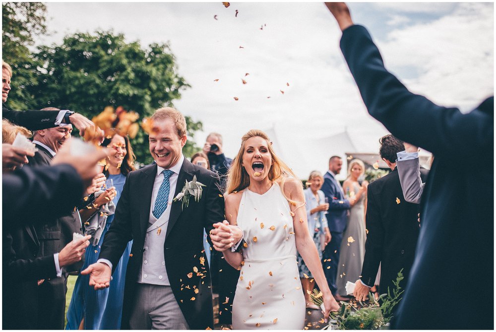 Bride and groom laugh as their wedding guests shower them with confetti