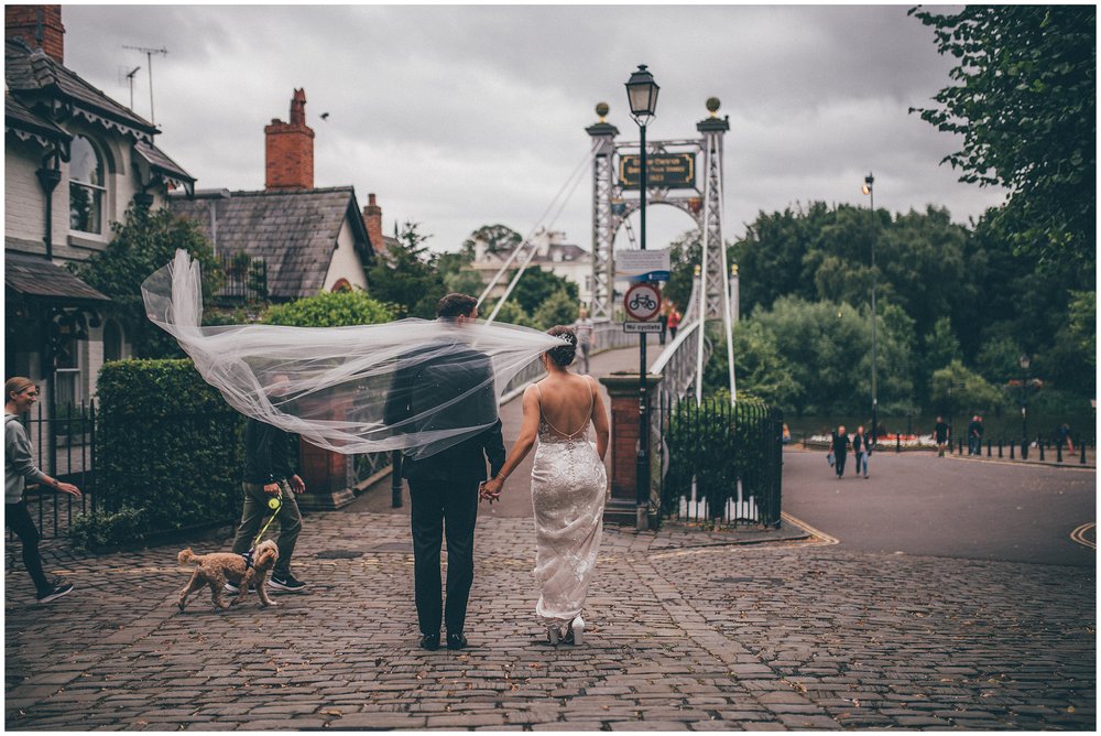 Bride and groom walk through Chester as her long veil blows in the wind