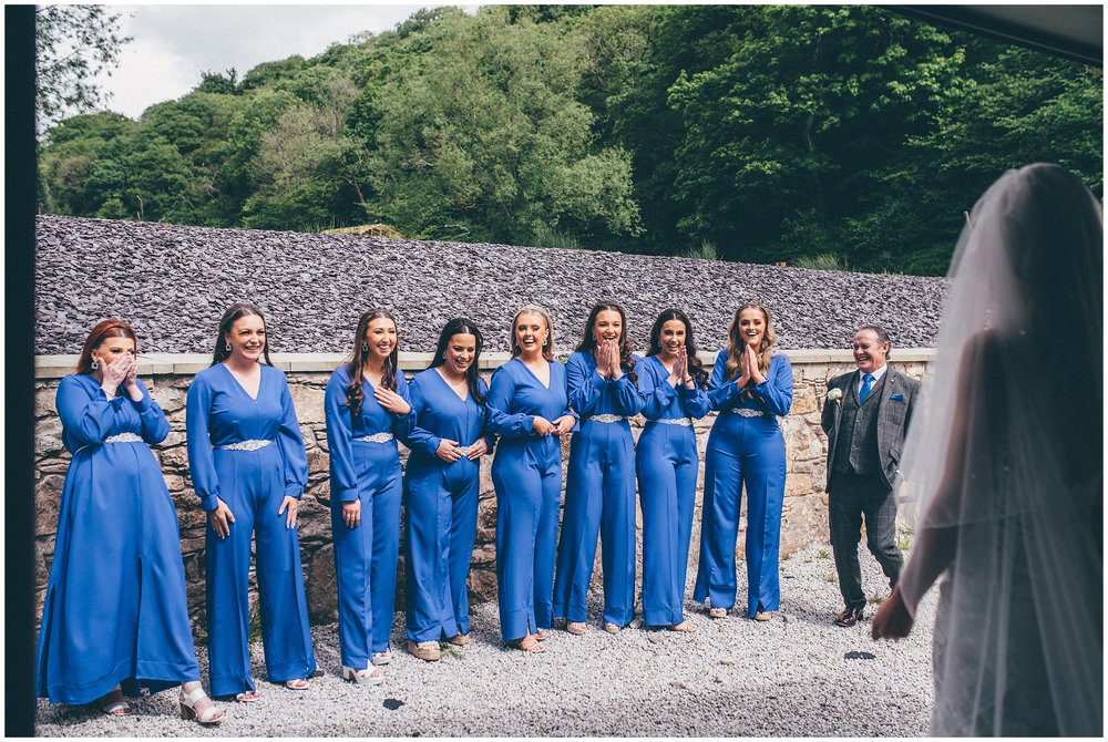 Eight bridesmaids in blue jumpsuits see the bride in her wedding dress for the first time