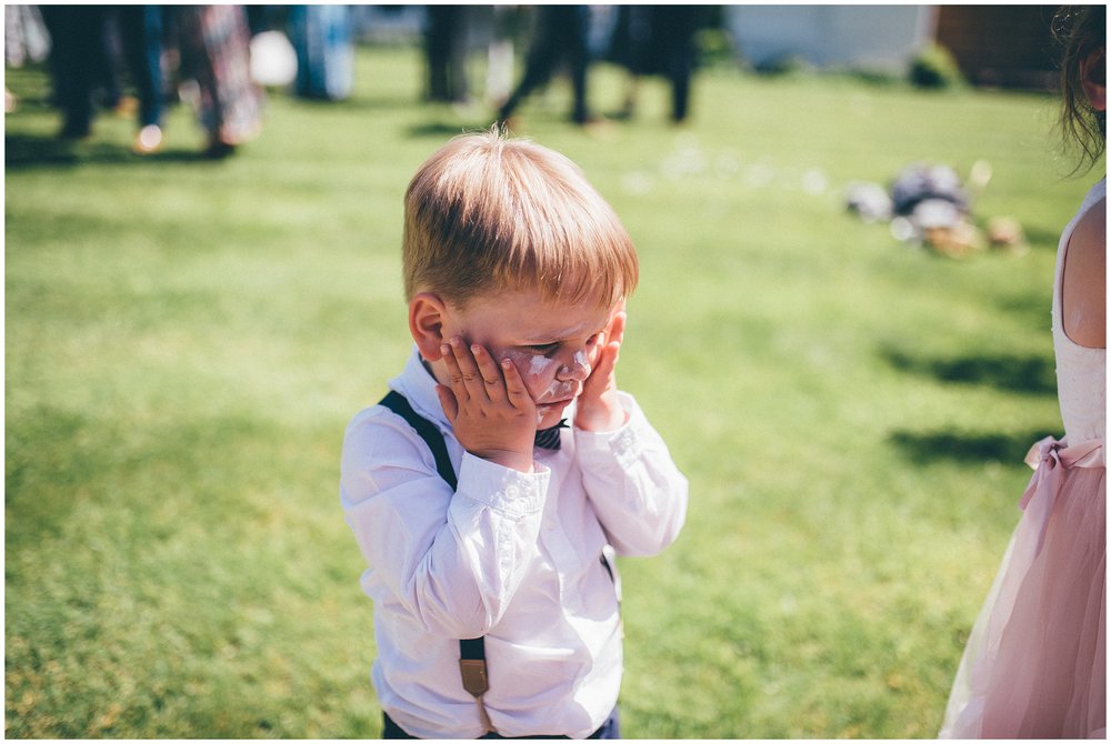 Little boy rubs suncream onto his face at Rowton Hall wedding in Cheshire