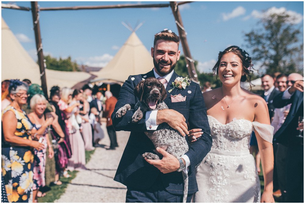 Bride and groom get confetti thrown at them whilst they hold their puppy at Skipbridge country weddings