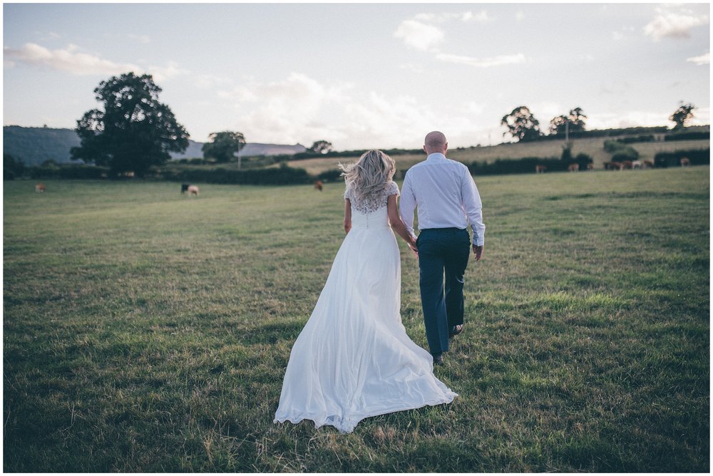 Bride and groom walks through the field of cows at Tower Hill Barns wedding venue