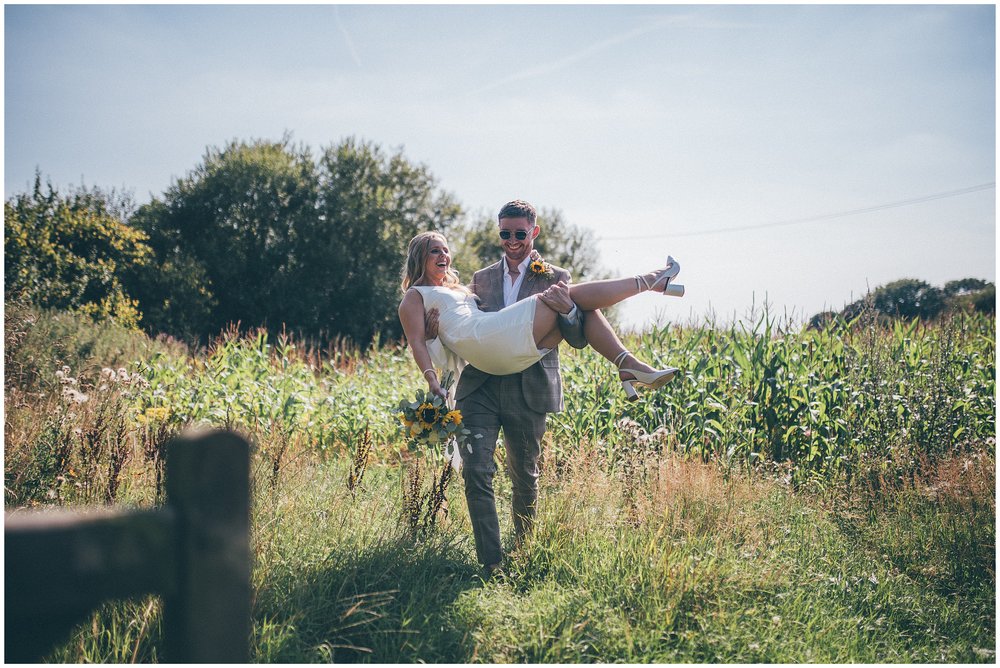 Groom carries bride through a field in Cheshire wedding