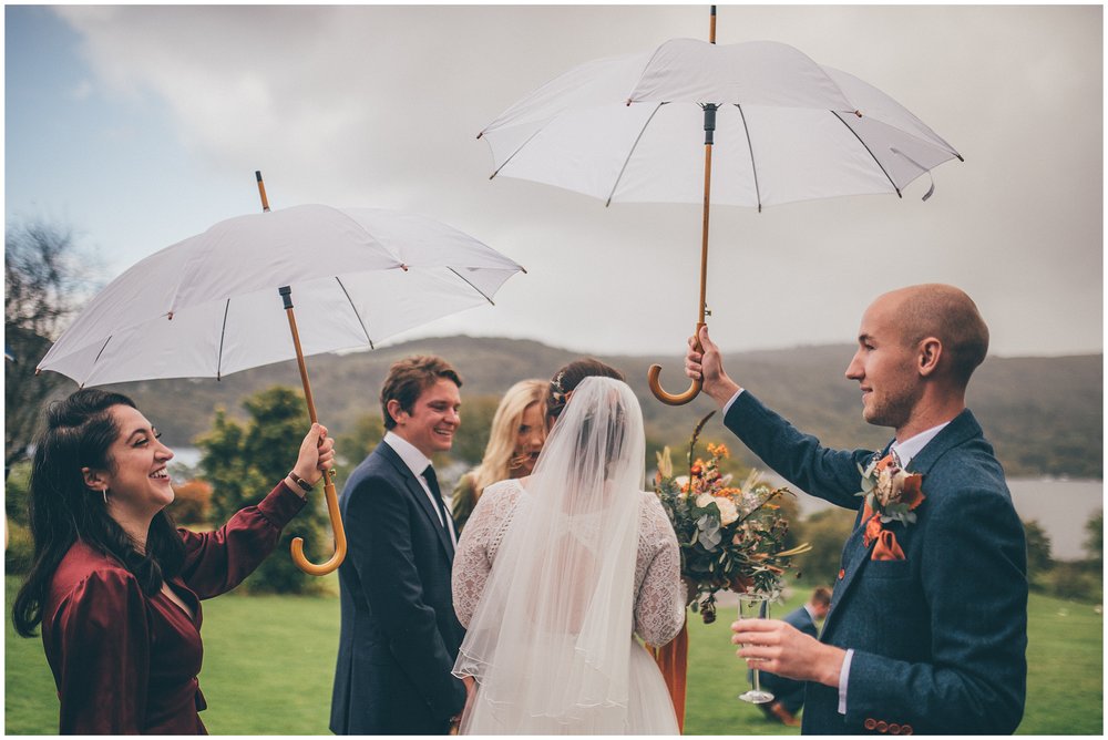 Wedding guests hold umbrellas above the bride at a Lake District wedding at Silverholme Manor