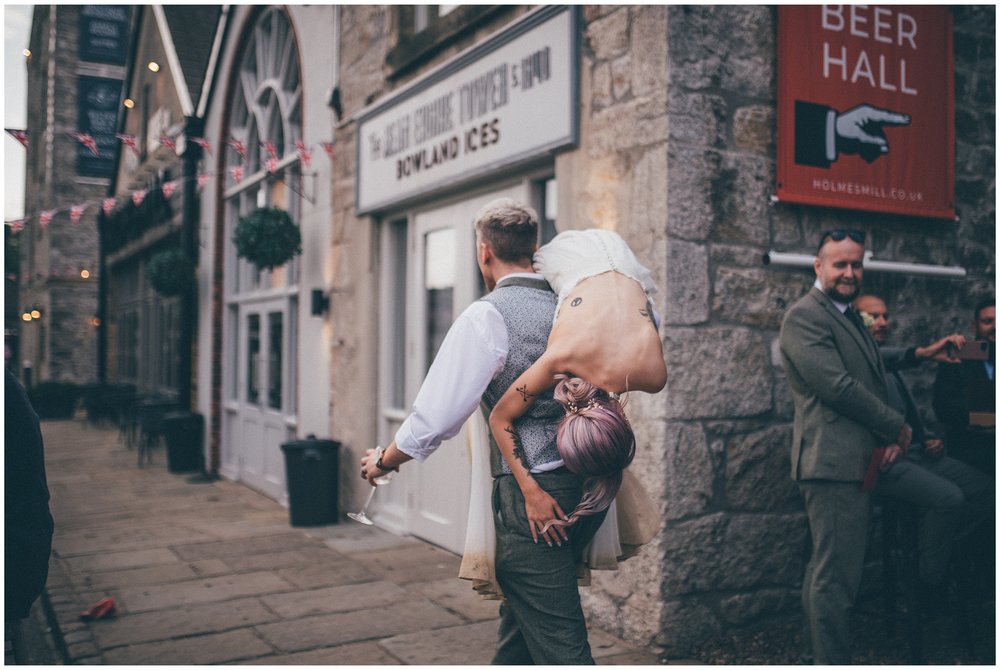 Groom carries his bride off over his shoulder at Holmes Mill wedding venue in Clitheroe
