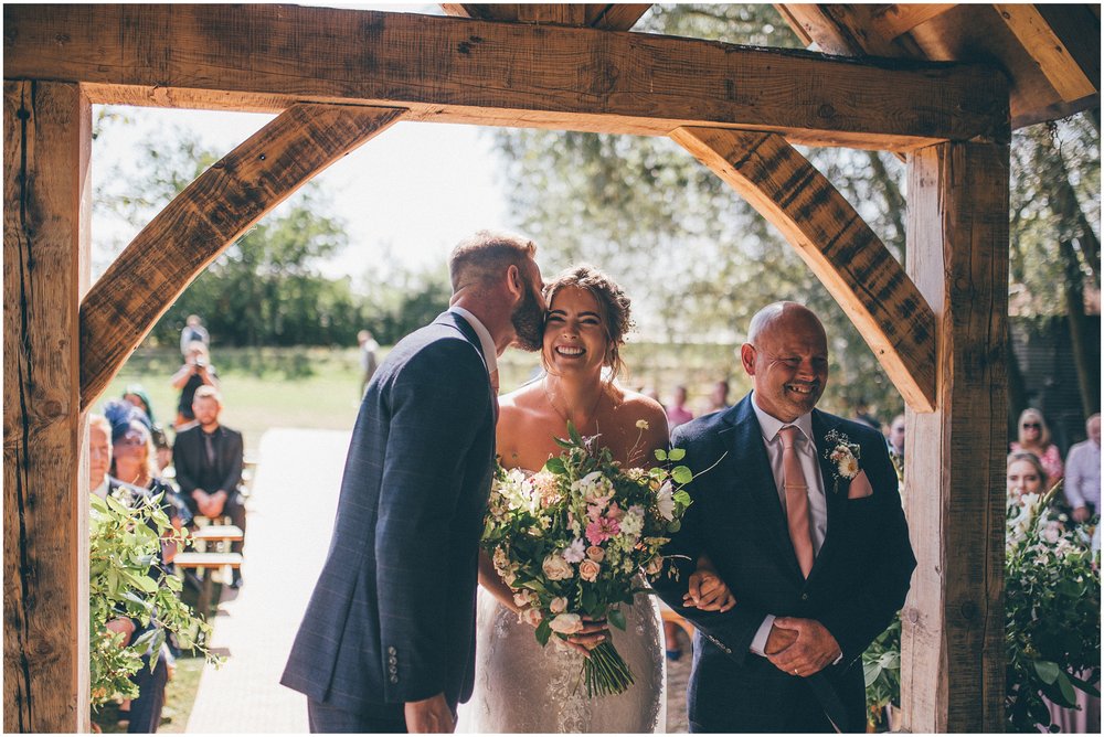 Groom kisses his bride as she reaches the top of the aisle with her dad at Skipbridge Country Wedding venue in Yorkshire