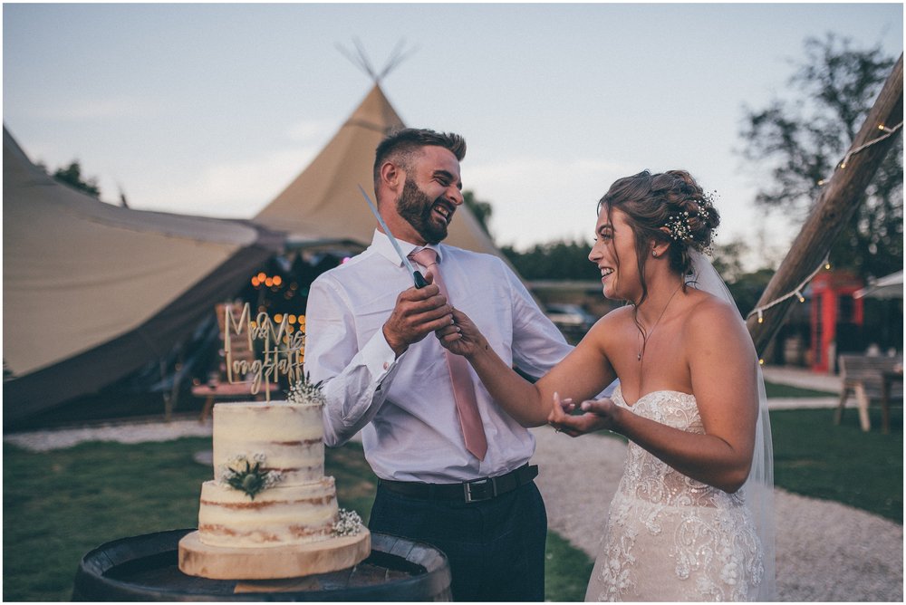 Bride and groom cut their wedding cake outside their summer tipi at Skipbridge Country wedding venue in Yorkshire