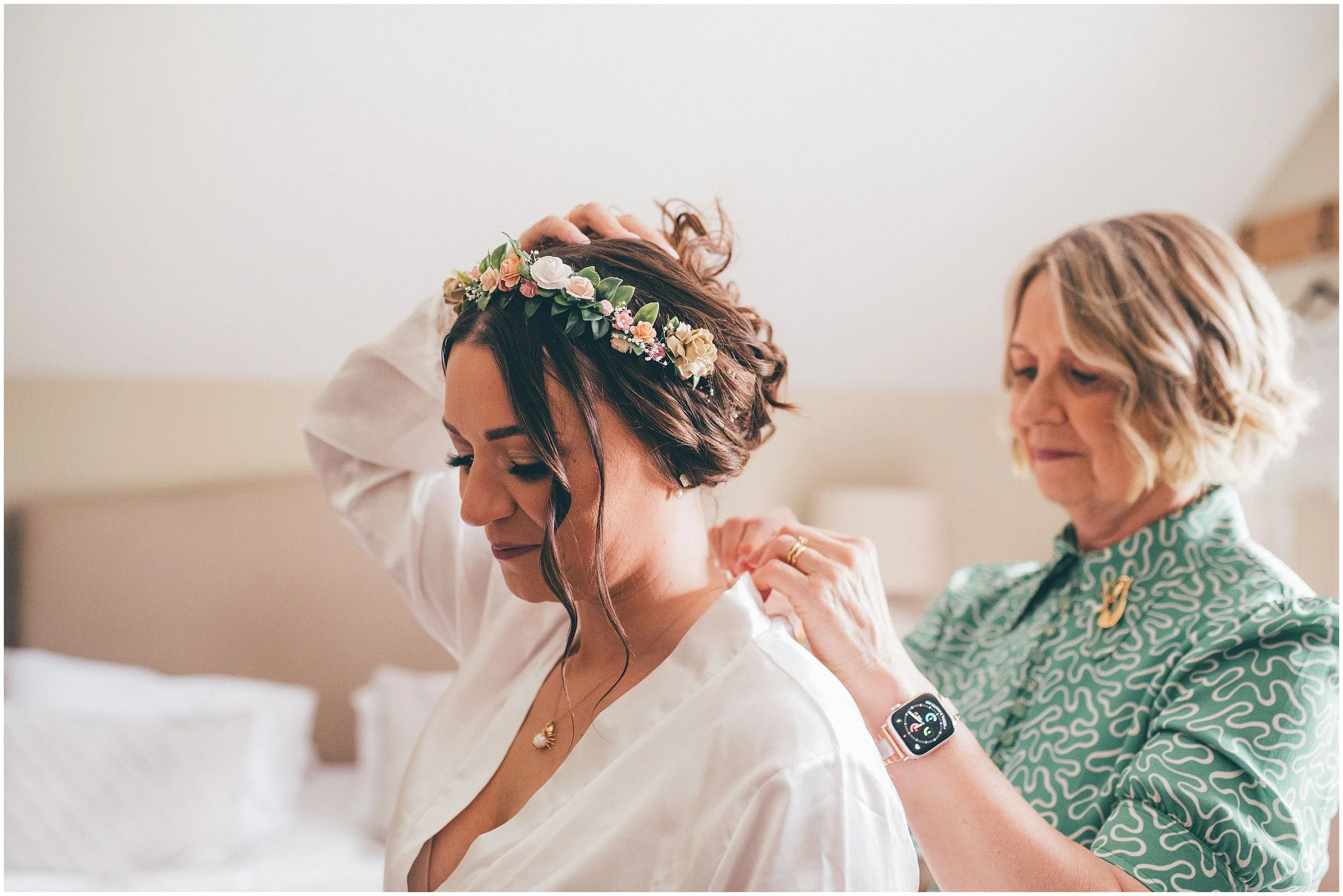 Bride wearing a flower crown get her necklace put on by mother-of-the-bride at Hobbit Hill wedding venue