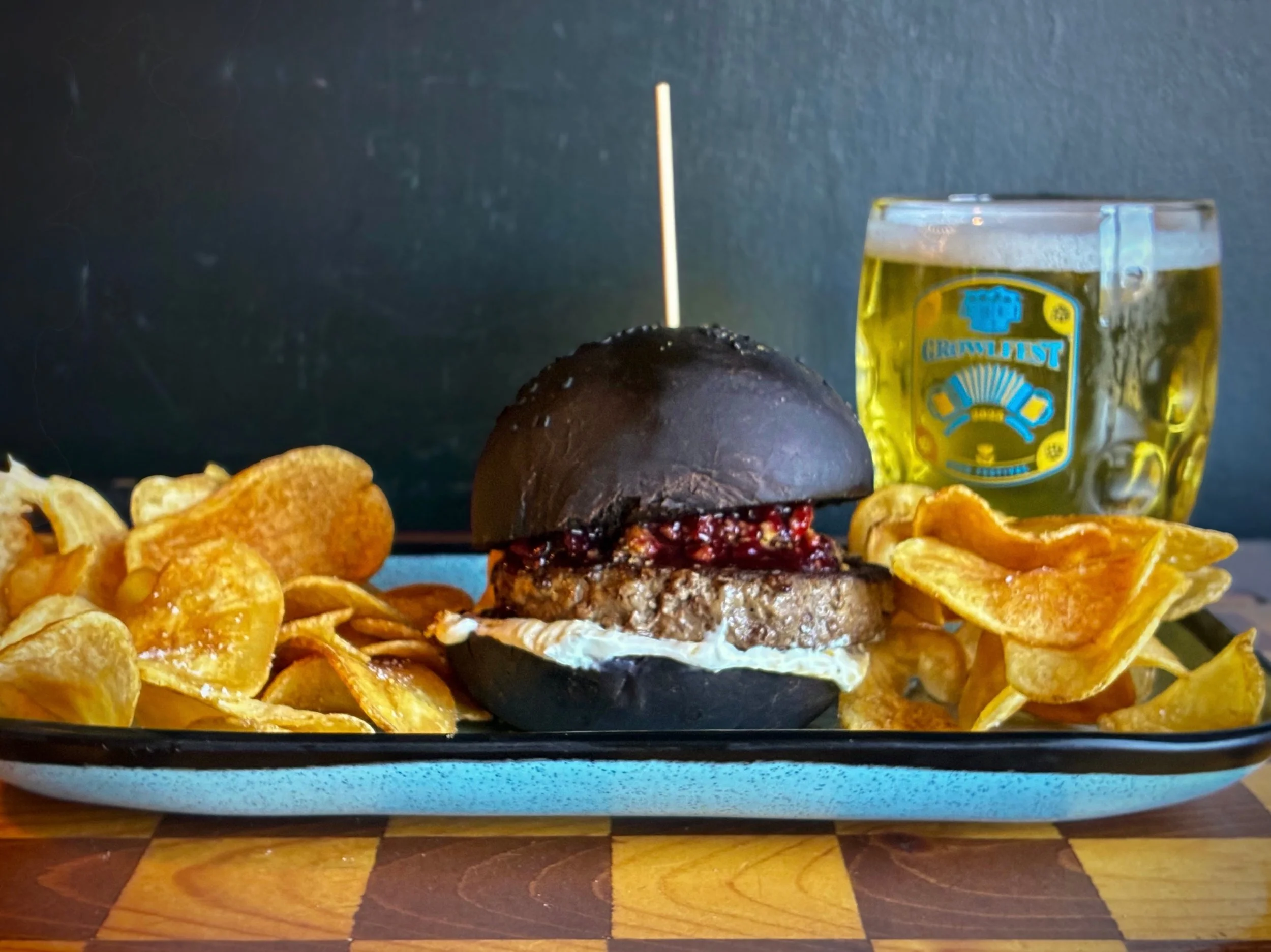 MURDER ON THE BURGER EXPRESS topped with goat cheese-cream cheese spread, cherry red wine compote, and crispy bacon graham crumble on a house black cocoa bun. 
Sandwich special available through Sunday during lunch, dinner, and brunch. 
Pair with GRE