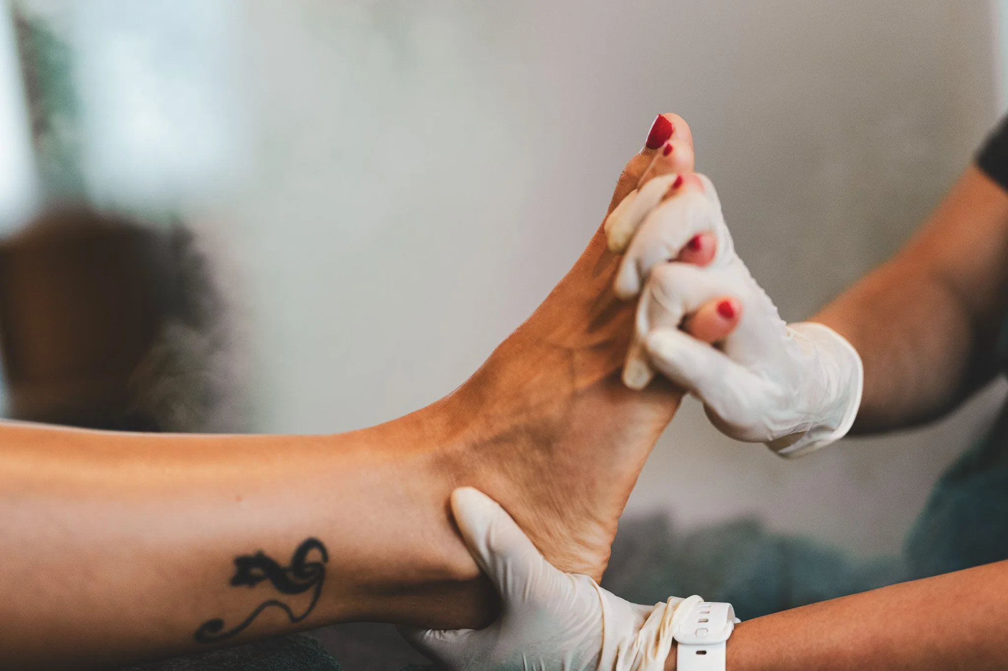 Two people with light skin holding hands; one with a tattoo of a seahorse on the wrist, and both wearing gloves, in a close-up shot.