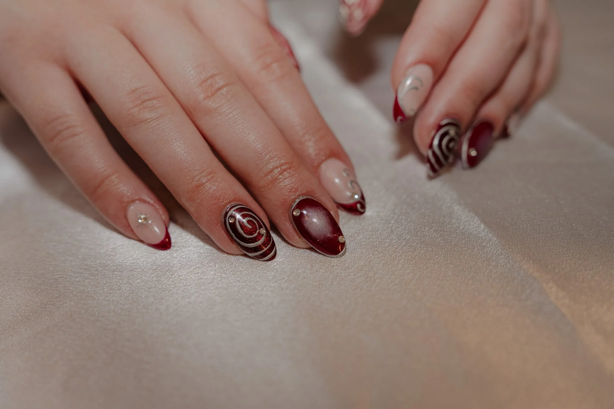 Close-up of hands with decorated fingernails resting on a beige satin fabric.