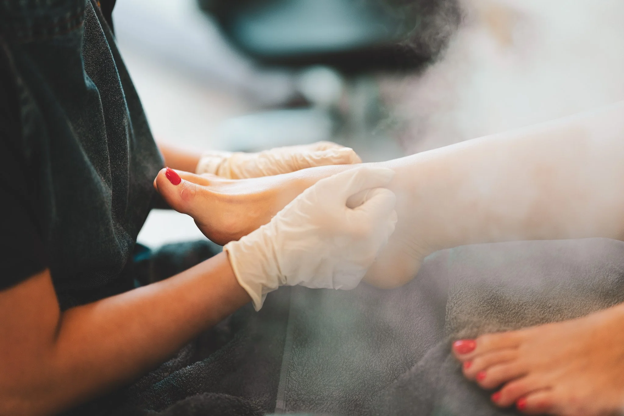A person in gloves checks another person's feet, which have red nail polish, at a spa or salon.