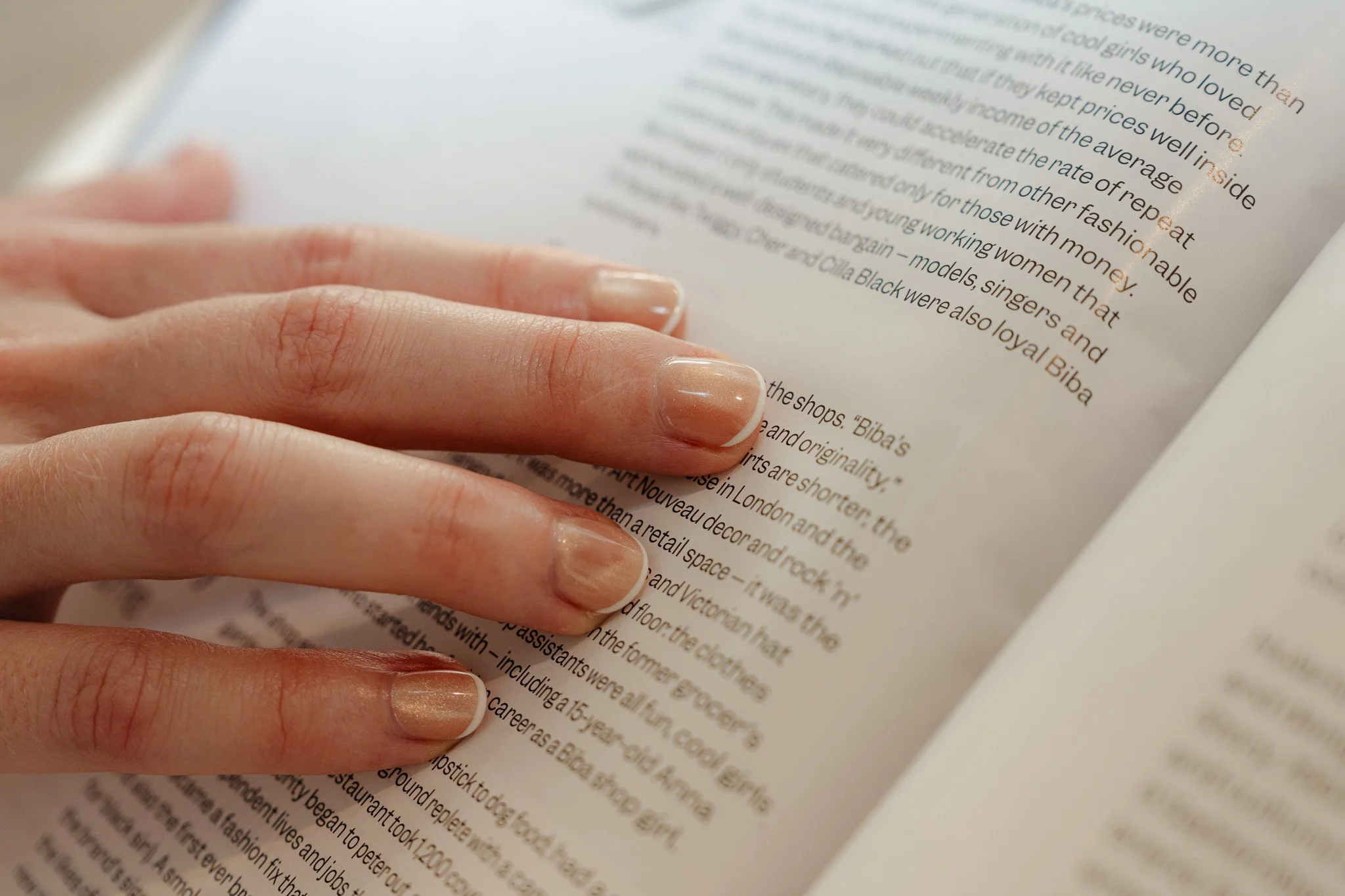 Close-up of a person's hand with neatly manicured nails holding a page of a magazine or book.