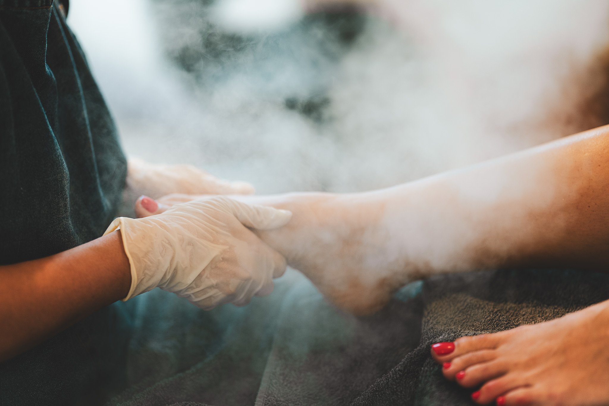 A person in a black shirt receives a massage with steam or heat therapy, while another person with red nail polish holds their leg.