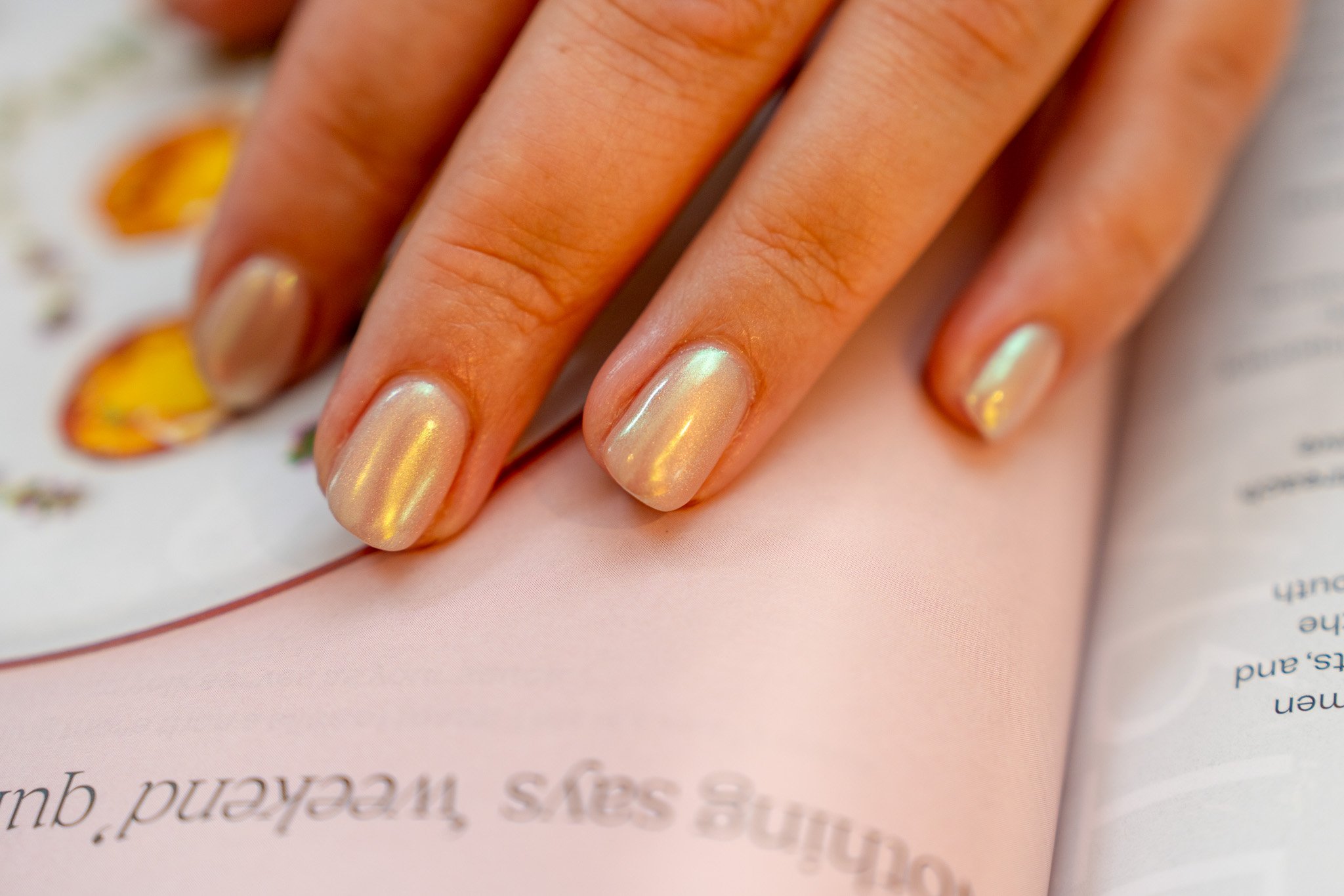 Close-up of a hand with iridescent, light-colored nail polish resting on an open magazine.