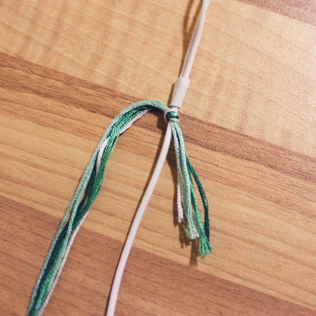 Cut your embroidery floss to 2.5 – 3 times the length of your headphone cord. Gather the ends and tie them around the base of the cord (just beneath the place where the cord splits in two). Be sure to leave a bit of a tail.
