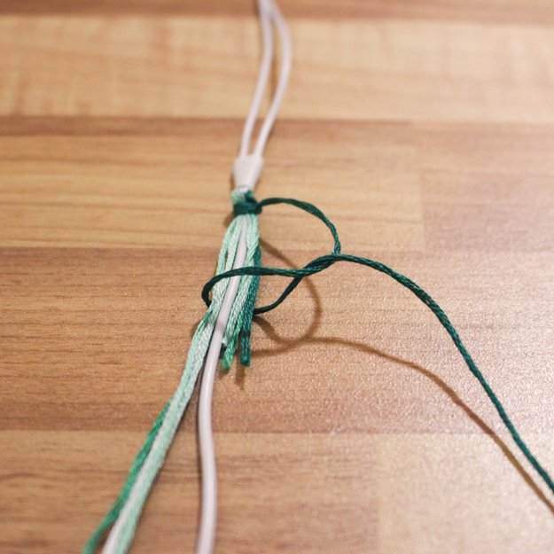 Separate your first color and knot it around the cord, the other strands, and the tail from the large knot. As you pull it tight, slide it up to the base of the large knot.