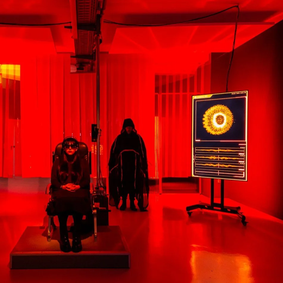 Kaksi mustiinpukeutunutta henkilöä punaisella valaistussa huoneessa.