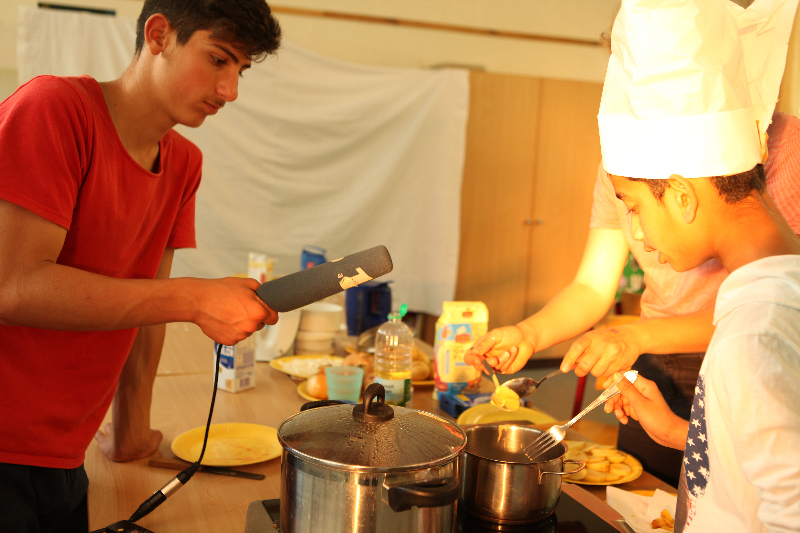 Geflüchtete und nichtgeflüchtete Kinder und Jugendliche inszenieren eine Kochshow über typisch deutsche und syrische Gerichte. Ziel war es, sich gegenseitig das Essen näher zu bringen und sich mit kulturellen Unterschieden und Gemeinsamkeiten auseinanderzusetzen.