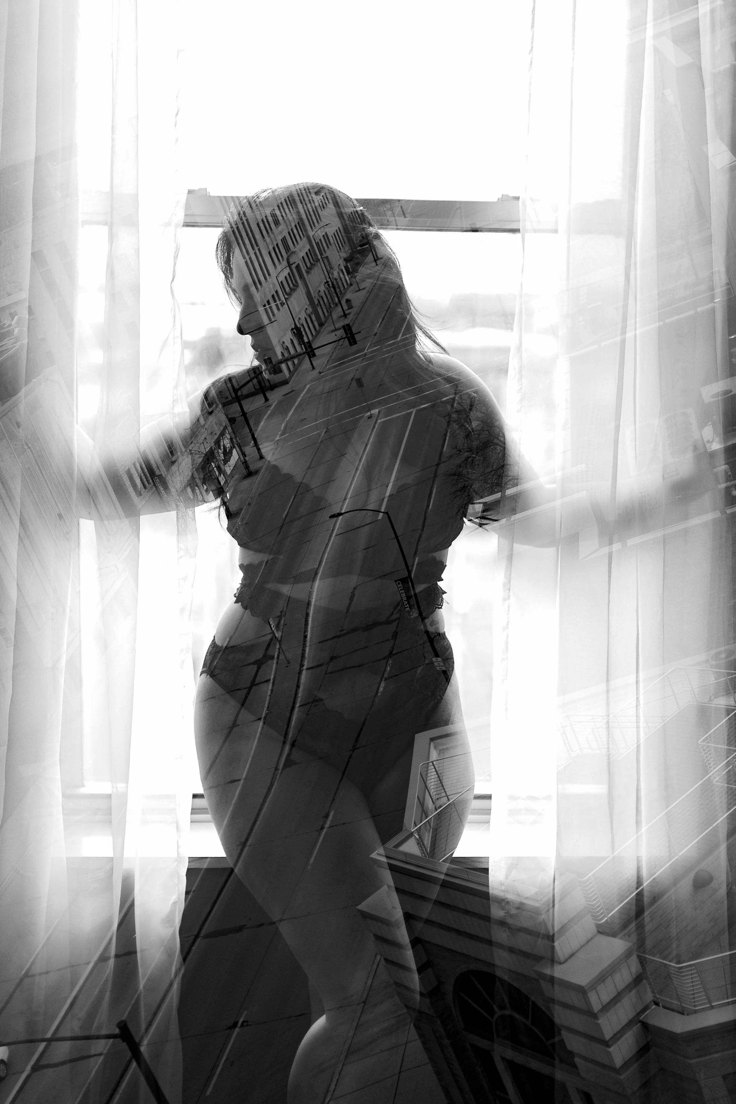 Black and white double exposure photograph of a woman standing by a window, with an overlay of city streets and buildings.