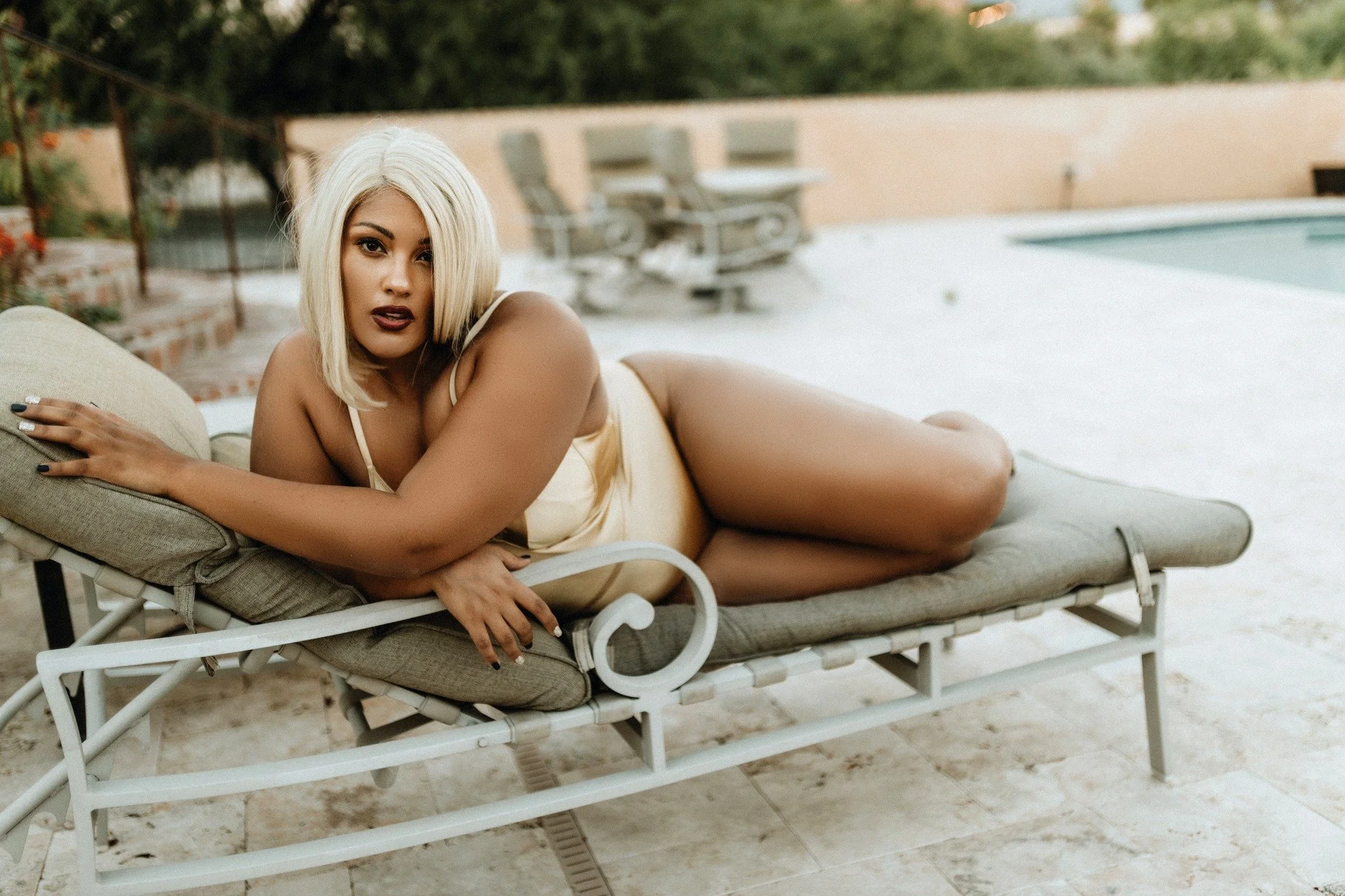 Woman with platinum blonde hair lying on a patio lounge chair next to a swimming pool.