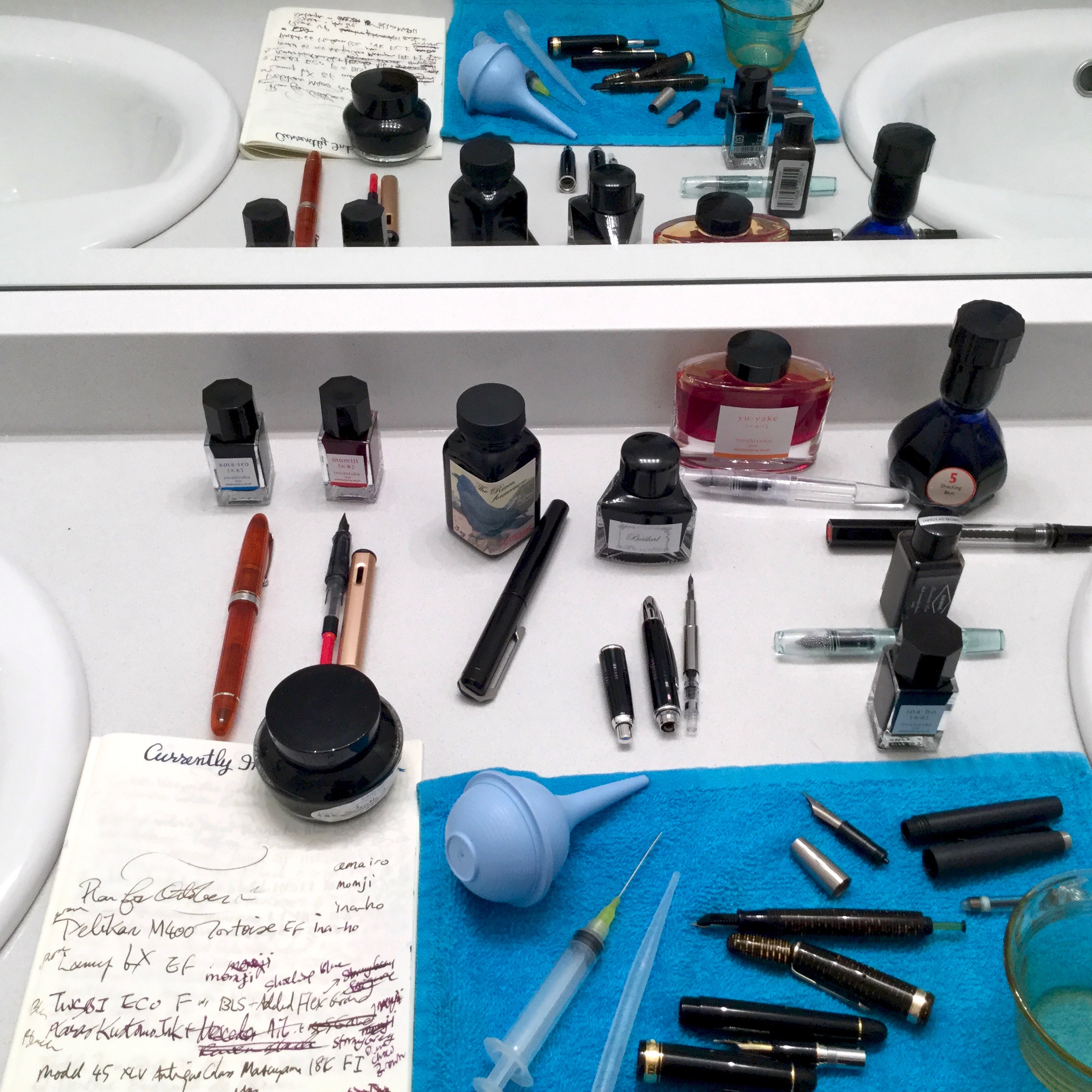 In foreground & mirror reflection, on top of blue towel: bulb syringe, blunt tip needle, cleaned and sorted pen parts