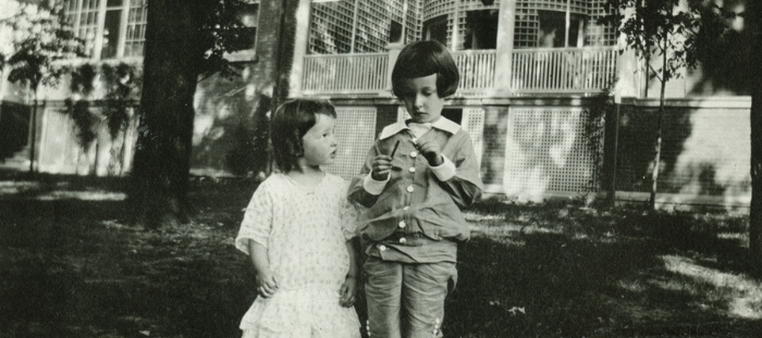  Historic photograph of Patty and IL Ellwood as children, standing outside the conservatory  Black and white photograph of Patty and IL Ellwood as young children  They are standing on the west lawn of the Ellwood House, with the conservatory seen in 