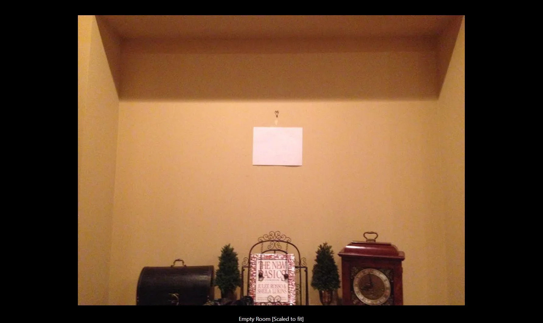 The client provided this photo (with 8.5x11 paper taped to wall for scale. It's a great shot because it includes just a touch of both walls and ceiling as well as the items on the furniture below where the art will hang.