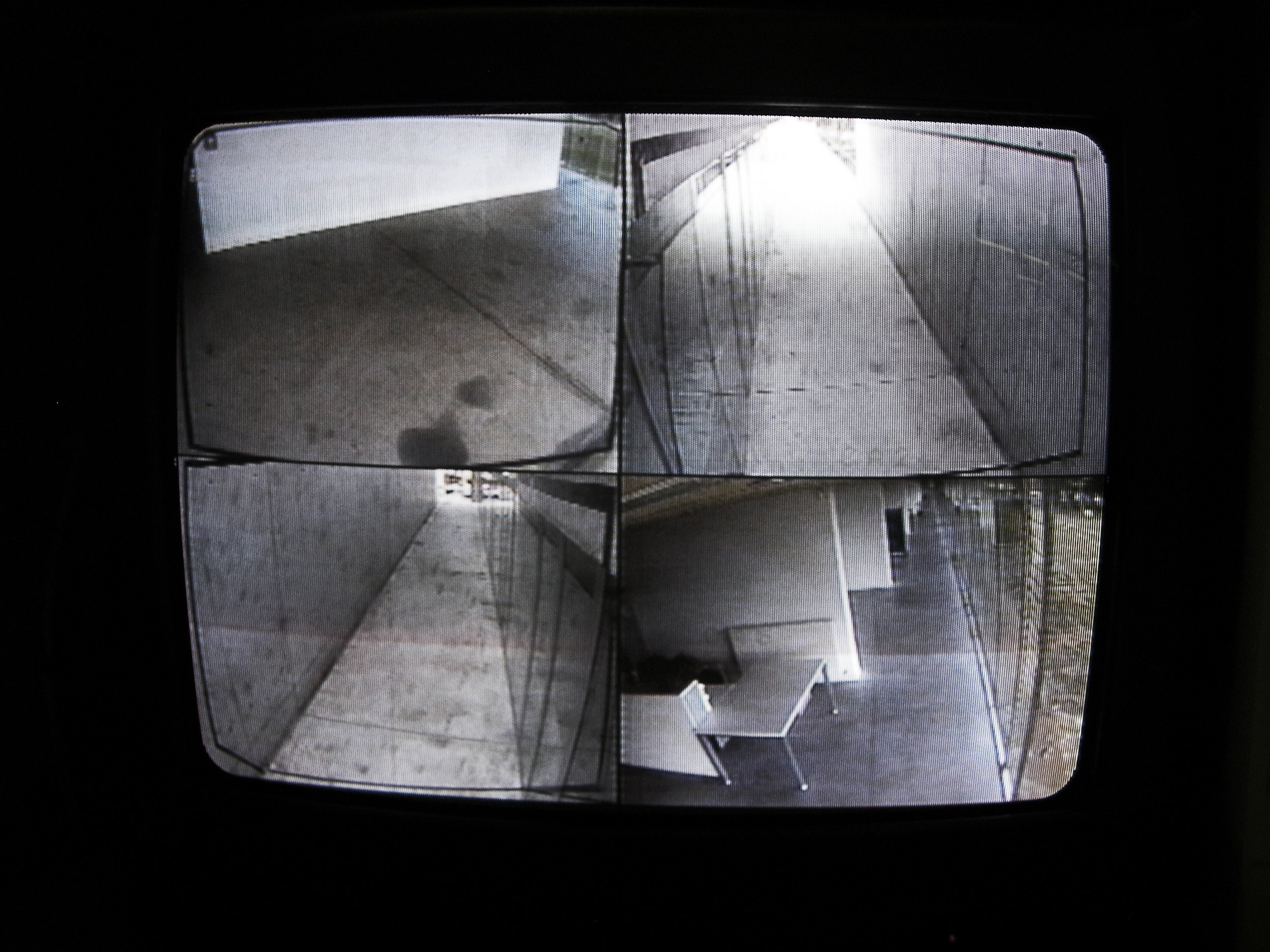 A black line is used to project the visual limit of the a two dimensional screen into the three dimensional reality, revealing the limit between surveilled and uncontrolled space. This thin line separates two areas with differentiated behavioral conducts: the space in the frame and the space out of the frame. By revealing the physical limit, the symbolic panopticon effect that the camera object projects is neutralized — The effectiveness of surveillance is cancelled once its limits become physical. Though a very simple gesture, the fuzziness of the areas that are being monitored disappears, revealing a sequence of potential spaces for transgression. The non-site specific installation “CCTV Spotlight”aims to disassemble the cinematic/spatial aspects of video surveillance through a minimal intervention. Video cameras are used to observe a particular area and are connected to a recording device. These sequences are then monitored through a screen by security personnel and then encoded on a digital support. The installation aims not only to demonstrate the existence of more immediate components, but also involve the architectural space and highlight the complexity of the system where the user has been implicated, in most cases, without being warned. This is a visual operation, non-site-specific, aims to be transferable to any area controlled by closed circuit television. A generic process is described and produced, providing a set of instructions to allow the installation to be reassembled in any video monitored public space.