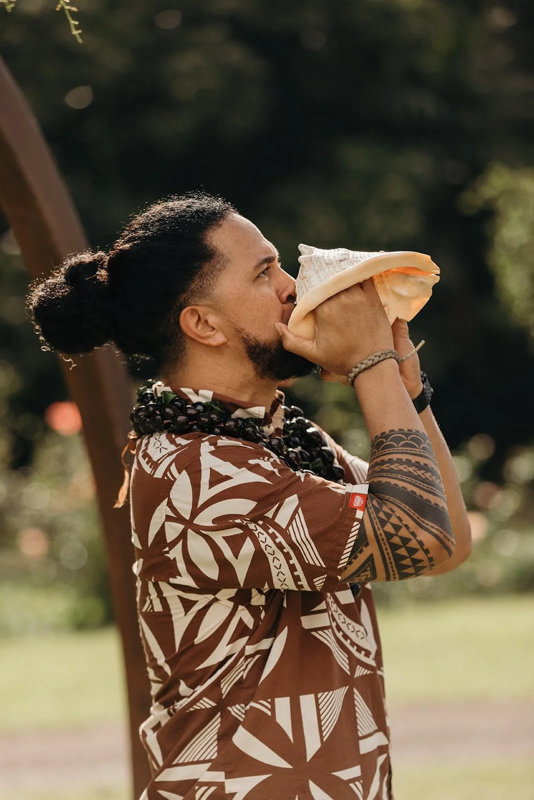 Hawaiian Officiant, Kahu Crichton Uale, blows conch shell at the commencement of a Hawaiian Wedding Ceremony in Waimea Valley.