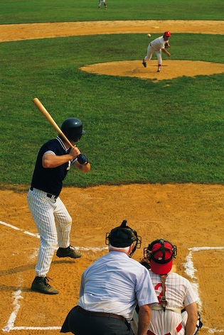 The pitcher pitches the ball. The referee and the catcher are behind the batter. ©iStock