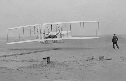 This is a photograph of the first flight, 17th December 1903. The plane is just lifting off the ground. Wilbur Wright is the figure on the ground. Orville Wright is the pilot. Photo courtesy of http://AviationHistory.info/