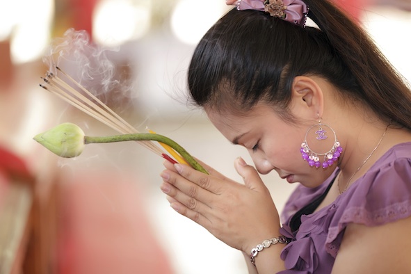 A Thai woman at a temple. She has incense sticks and a lotus bud. Getty Images