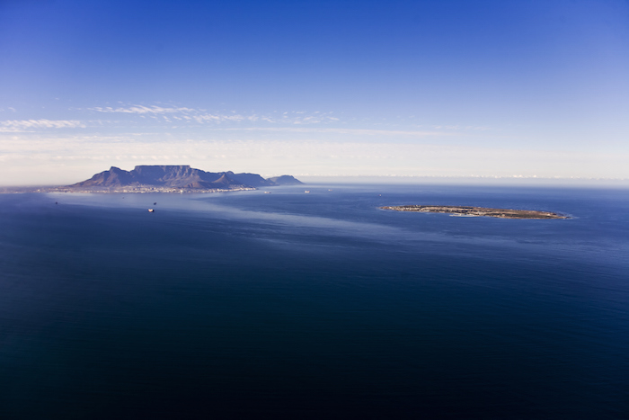 Robben Island (right) is a small, flat island off the coast of Cape Town, South Africa. Cape Town, at the foot of the famous Table Mountain, is on the left. Photo ©iStock