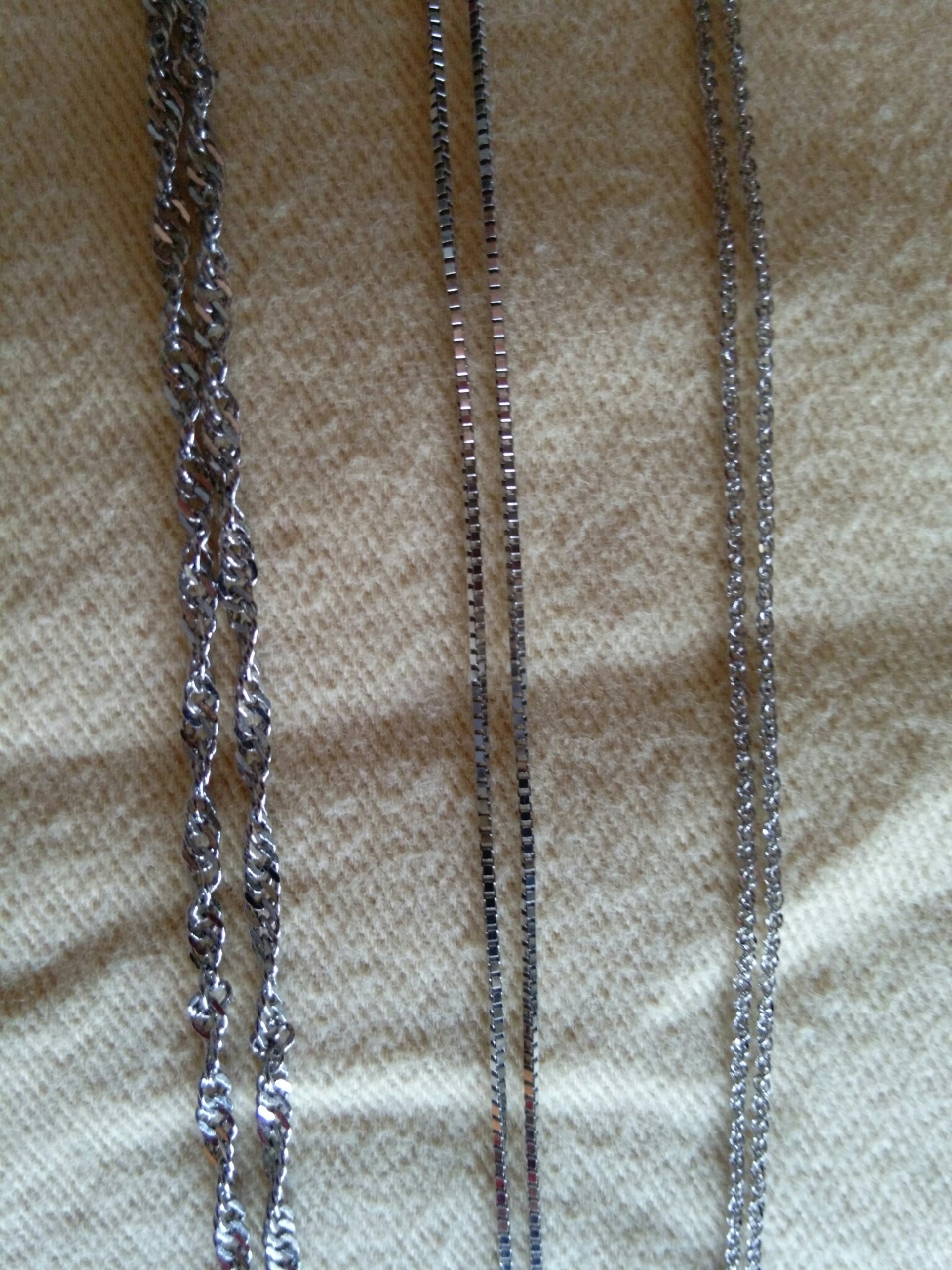 The necklace in the middle is 14k gold, the wider necklace on the the left is 14k gold-filled, and the necklace on the right is rhodium-plated sterling silver. The gold-filled necklace is almost indistinguishable from the 14k gold necklace. The rhodium-plated sterling silver is whiter and brighter. This beautiful necklace looks like white gold when worn alone, and one can only spot the difference when it is placed directly next to 14k gold.