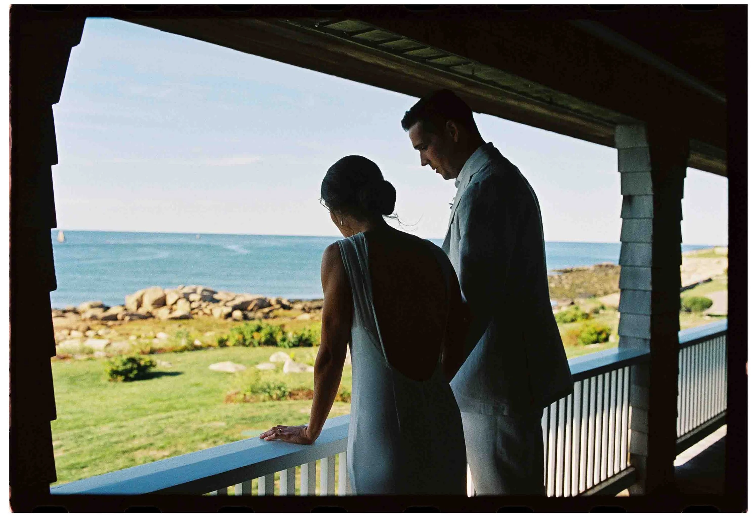 wedding couple on porch look out to the atlantic ocean at family home in gloucester