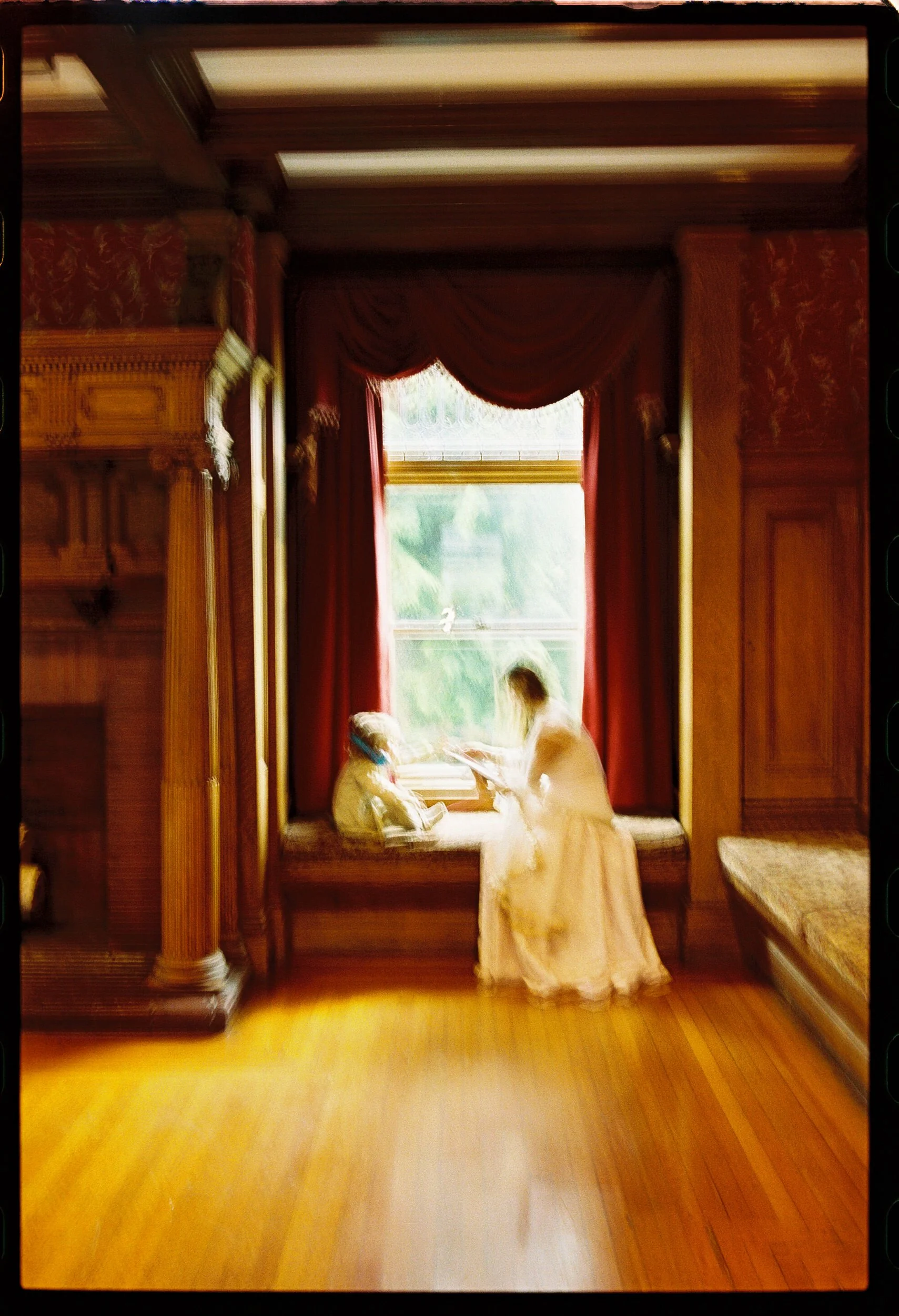 A newlywed in a wedding dress sitting in a nook by the widow with a child
