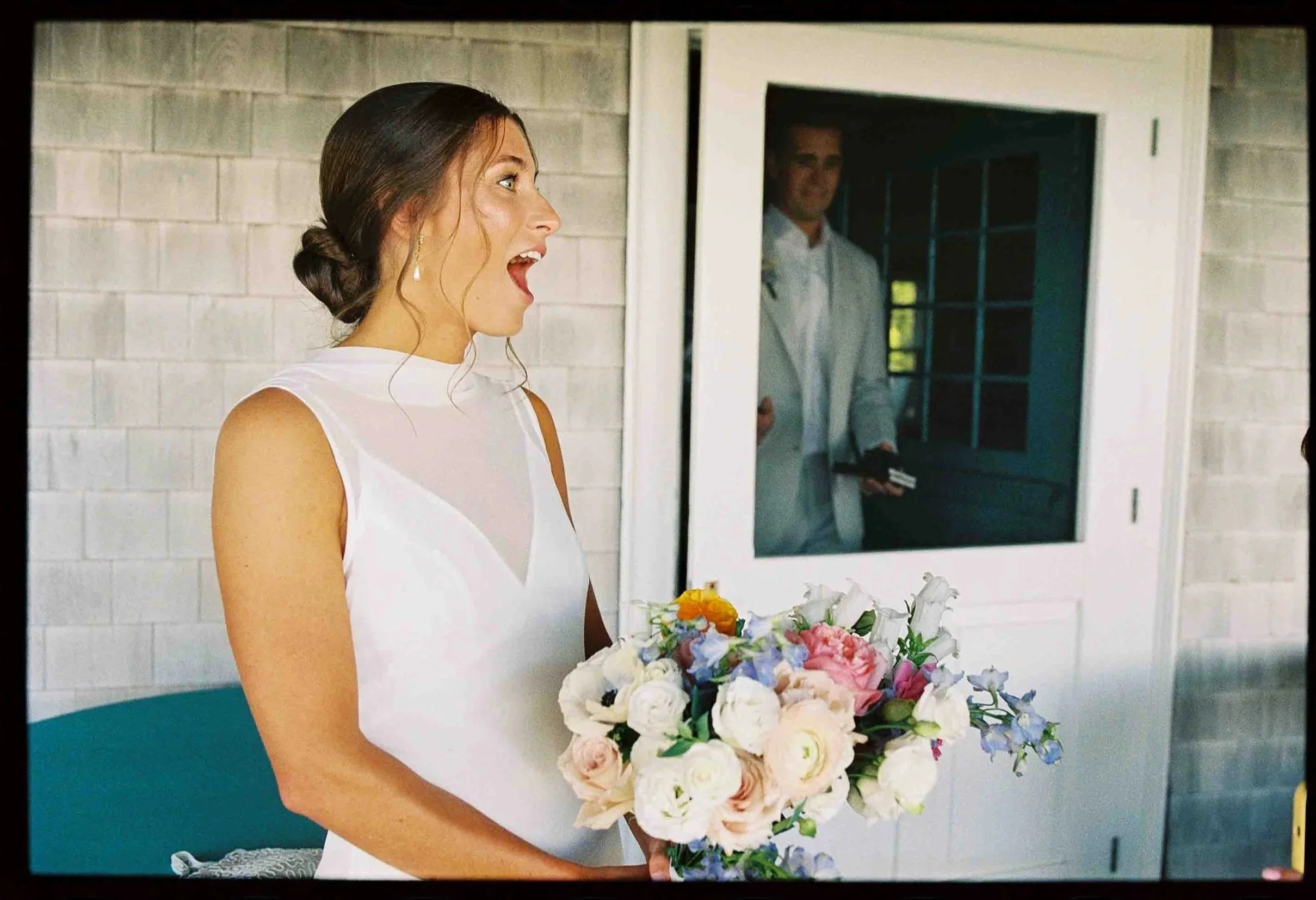 Bride holding bouquet as groom comes out through the door. 