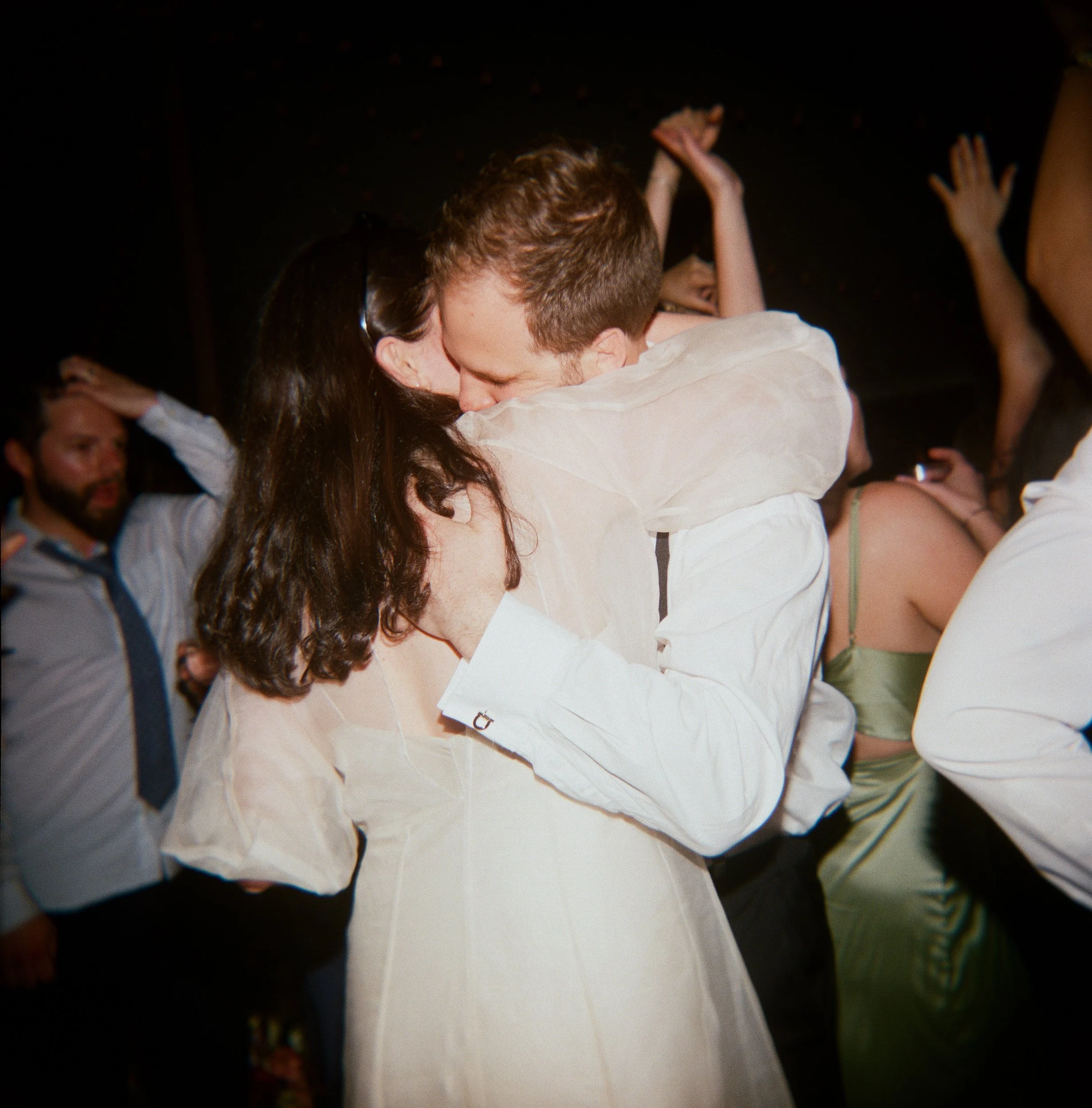 Newlyweds hugging with their guests dancing around them