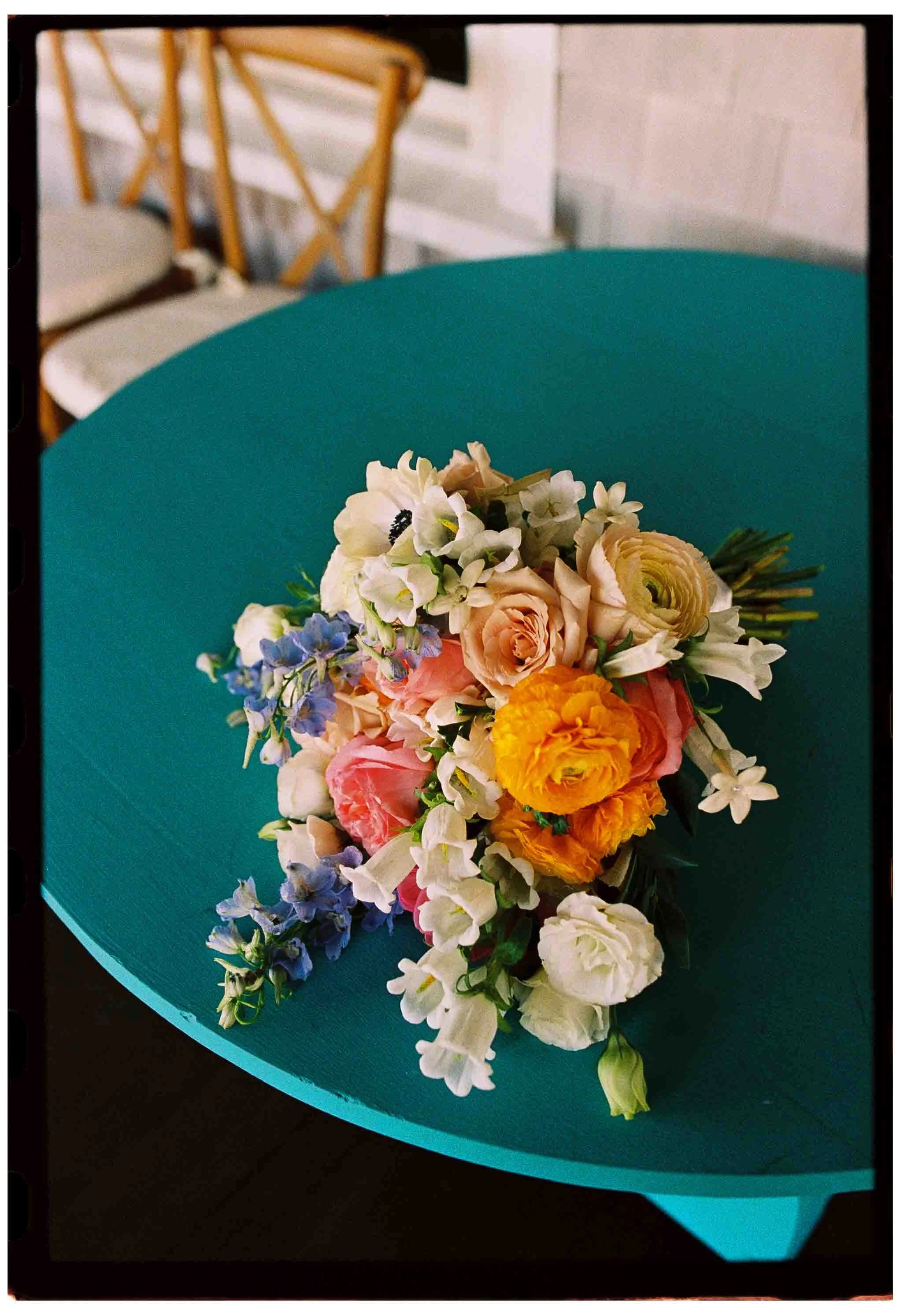 colorful bridal bouquet with blue orange and punk flowers on a turquoise table